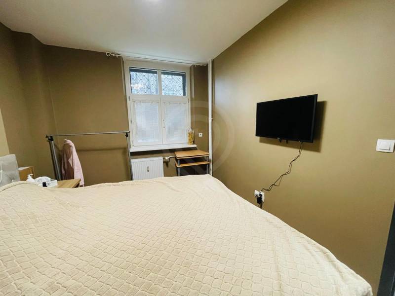 Bedroom in a 2-room apartment with a TV on the wall, a desk, and a hanging system.