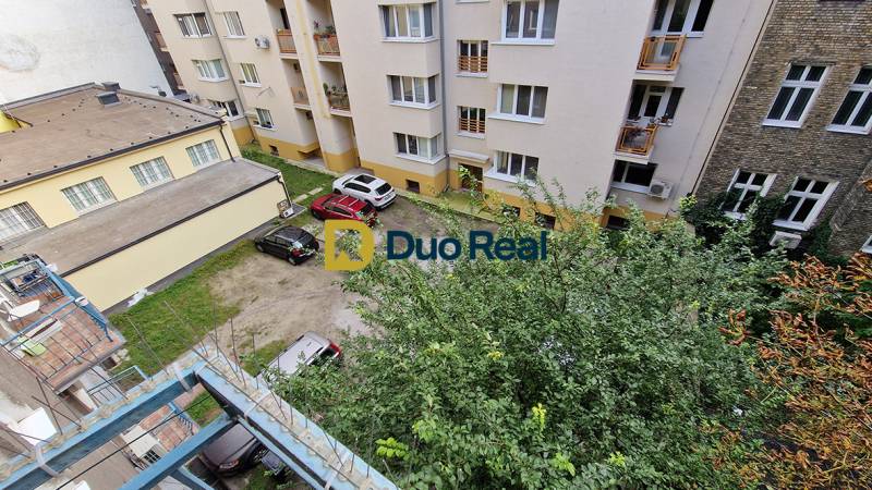 A view of the courtyard of apartment buildings with a parking lot and greenery on Grosslingova Street.