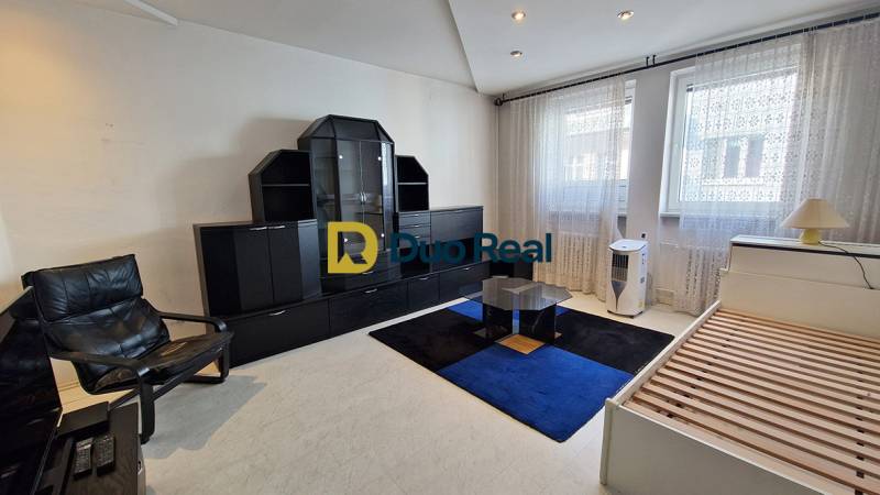 A room in a 3-room apartment with black furniture, a bed, and a chair.