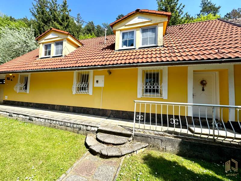 A family house in Vrbovce with a yellow facade, a red roof, and a front garden.