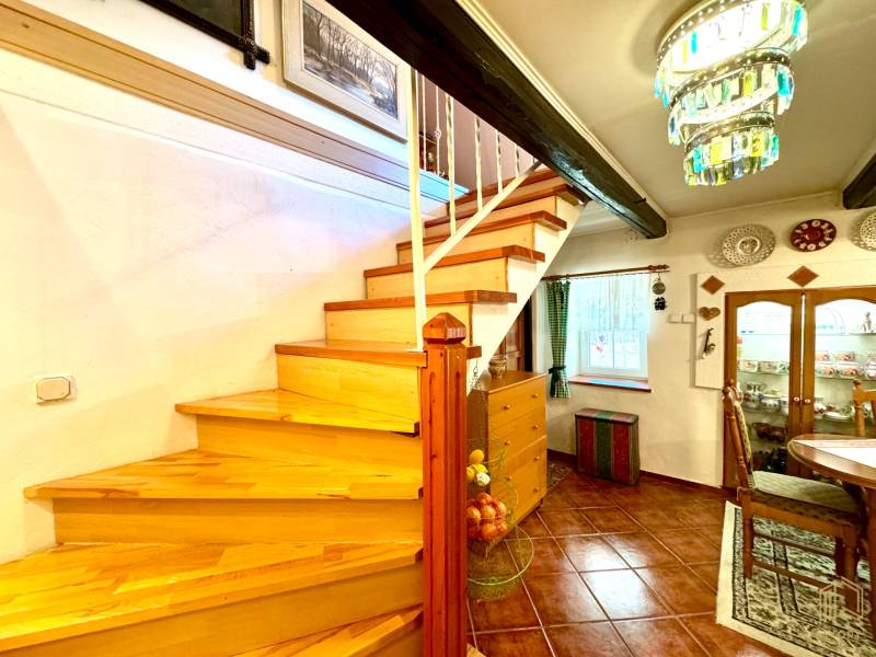 A staircase with a wooden decor, a dining table, a display cabinet, and a chandelier in a family house.