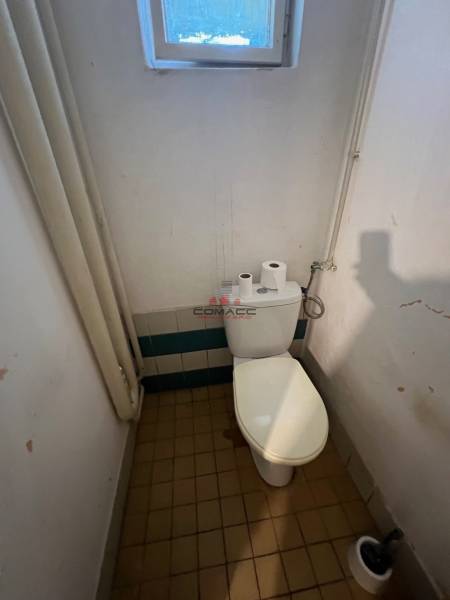 A bathroom with a toilet in a family house, includes a window, tiles, and toiletries.