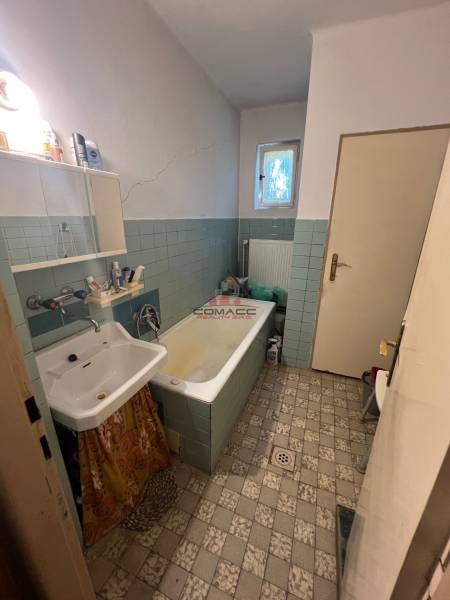 A bathroom in a family house with an old bathtub, sink, and tiles.