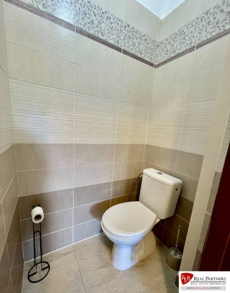 Bathroom in a 2-room apartment with a toilet, beige tiles, and decorative cladding.