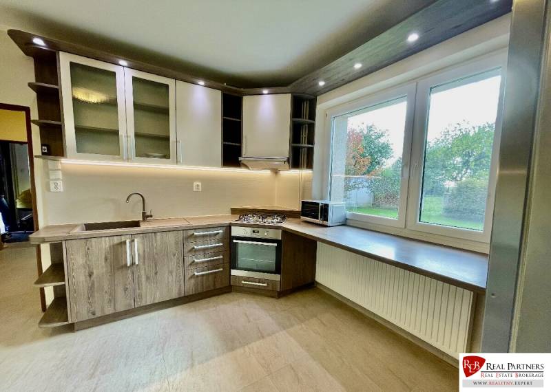 A kitchen unit in a 2-room apartment with a wooden decor floor and a large window.