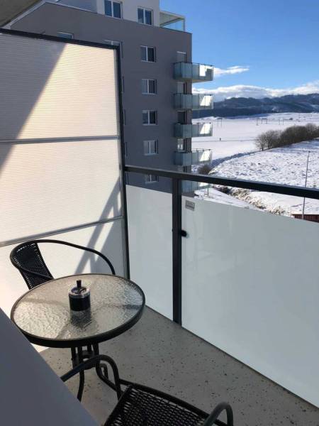 A balcony of a studio apartment in Poprad with a view of the snowy landscape and a residential complex.
