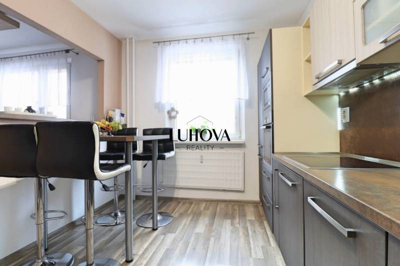 A kitchen with bar stools and a wooden decor floor in a 3-room apartment.