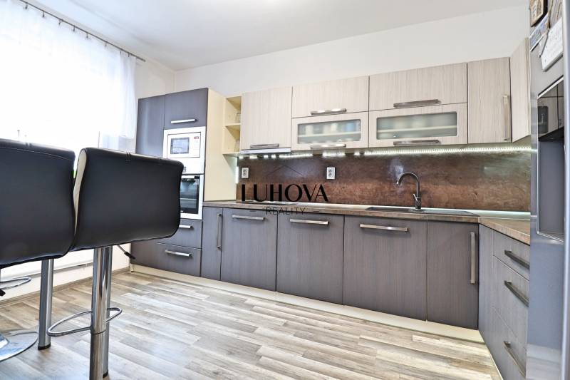 A kitchen with wood-patterned flooring in a 3-room apartment with built-in appliances and bar stools.