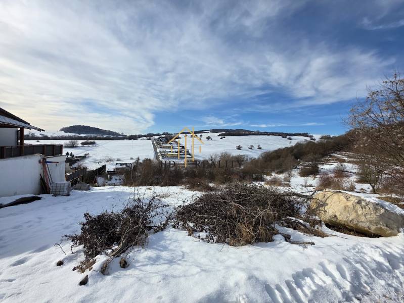 A snowy landscape with residential plots in Horná Mičiná, set in gentle hills.