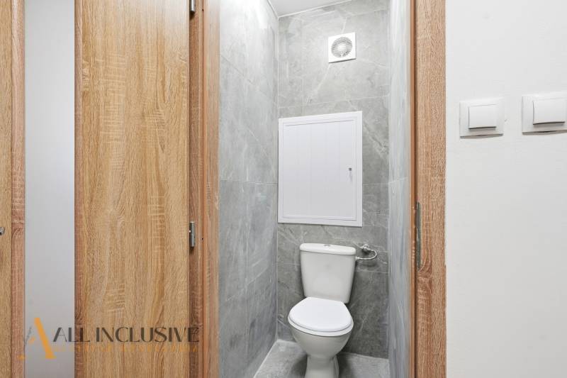 A toilet with wooden doors, gray walls, and a fan in a 3-room apartment.