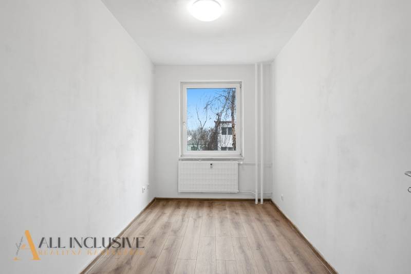 A bright room in a 3-room apartment with a wood-patterned floor and a window on the wall.