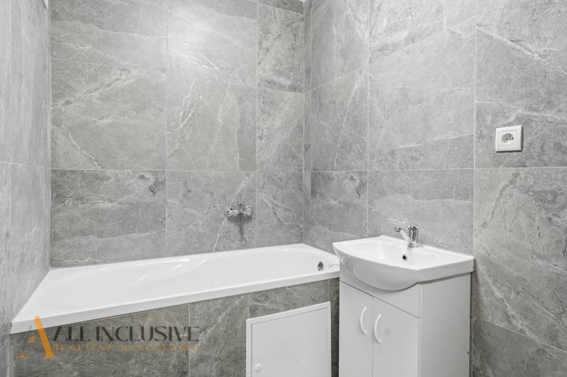 A bathroom with a bathtub and a sink in a three-room apartment with gray tiles.
