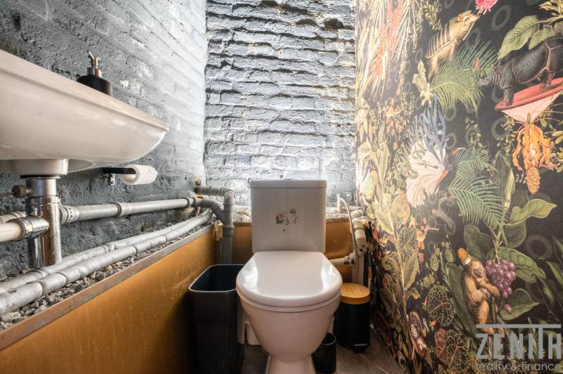 A small restroom with a sink, colorful wallpaper, and visible pipes in a dining area.