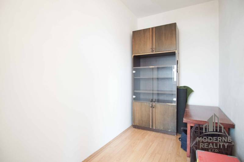 A room in a 3-room apartment with a wood-patterned floor and a cabinet.