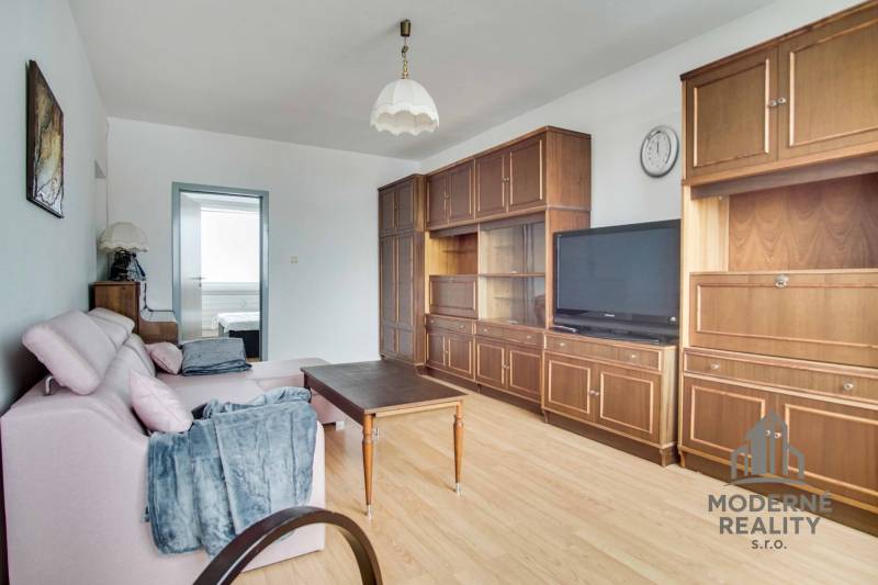 Living room in a three-room apartment with a wooden decor floor and older furniture.