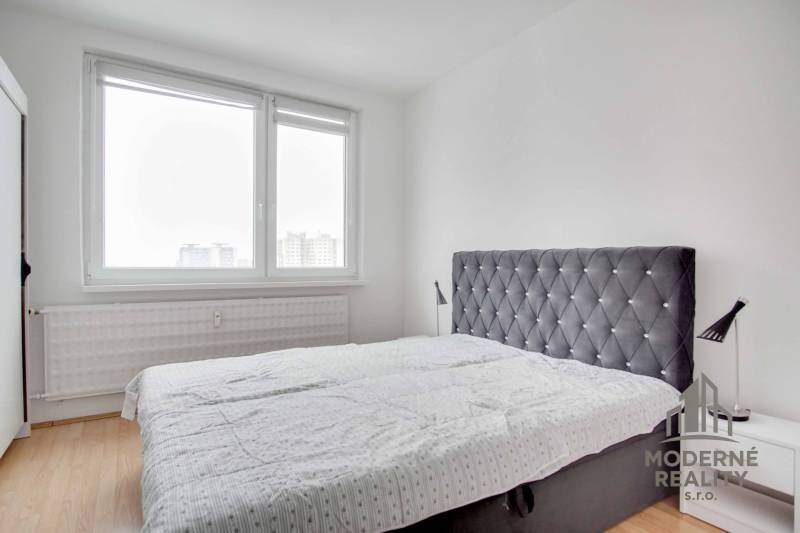 Bedroom with a large window, a simple bed, and a wooden decor floor in a 3-room apartment.