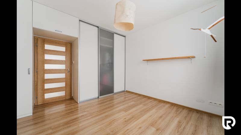 A room in a 2-room apartment with a wooden decor floor, a built-in wardrobe, and wooden doors.