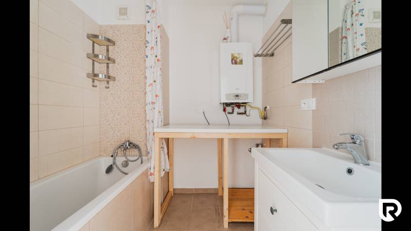 Bathroom with a bathtub in a 2-room apartment, with a wooden table and a gas boiler.