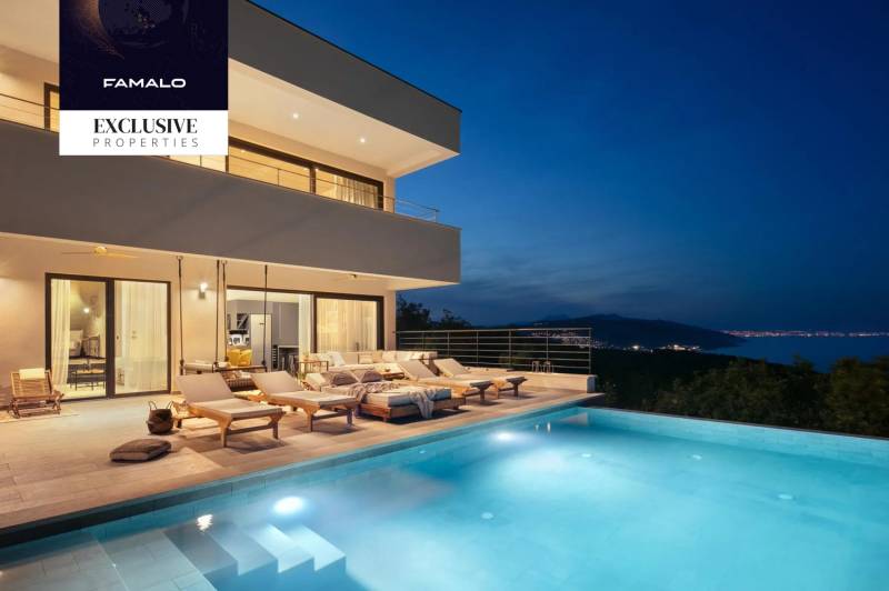 Villa with a terrace and pool, with a night view of the illuminated coastline.