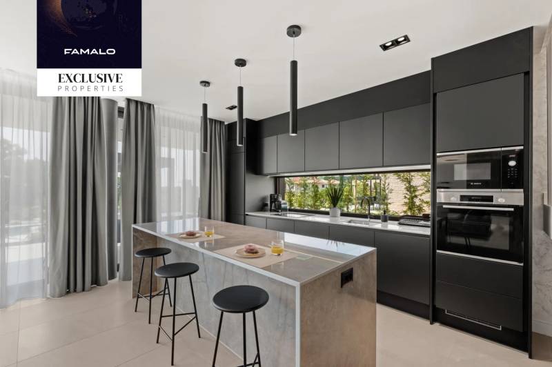 A kitchen in a villa with a stylish sharp design, a large island, and black cabinets.