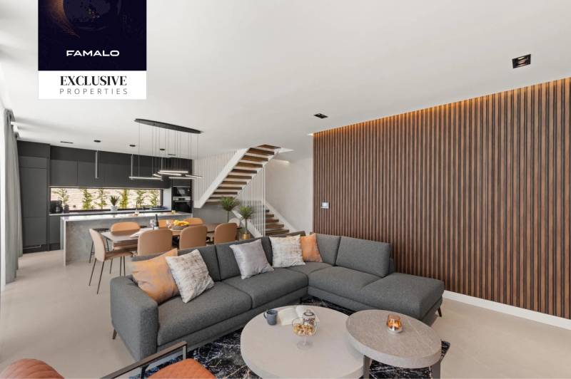 Interior of a villa with a corner sofa, open kitchen, and wooden decor on the wall.