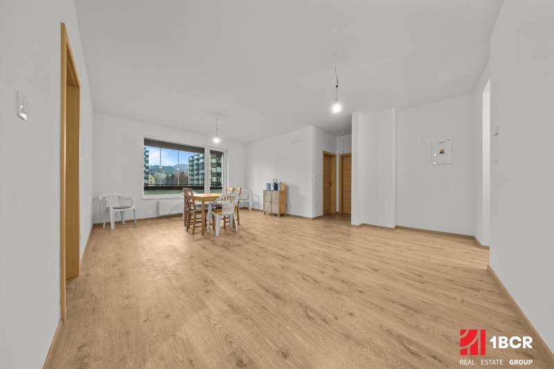 A bright living room in a three-room apartment with a wood-patterned floor and simple furniture.