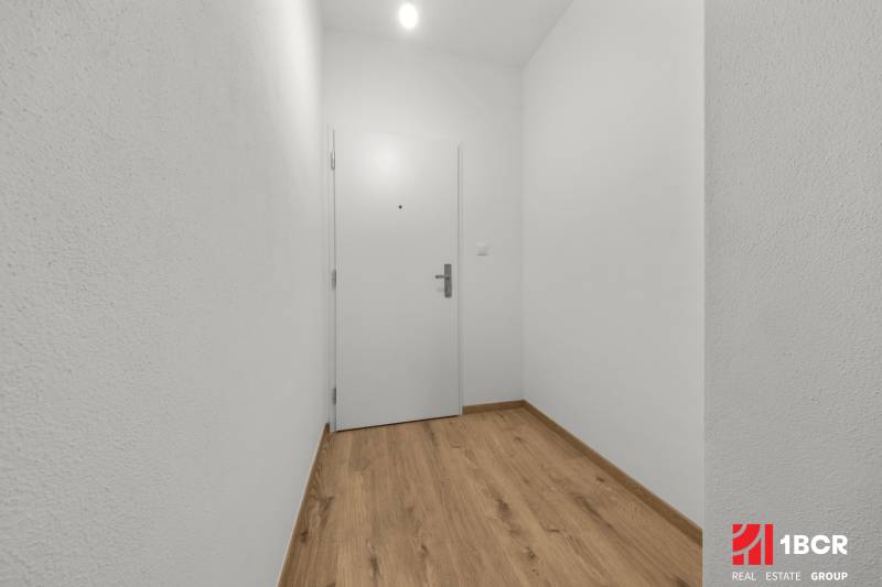 A hallway in a 3-room apartment with a wood-patterned floor and white walls.