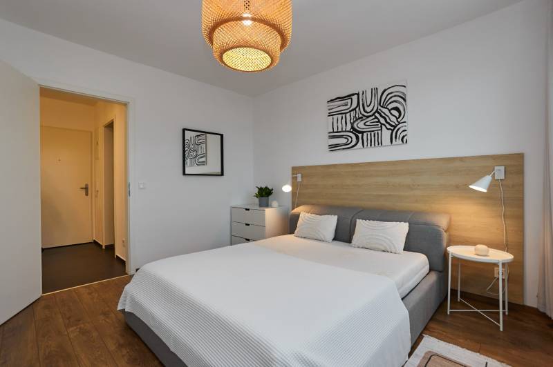 Bedroom in a 2-room apartment with wood-patterned flooring, simple furniture, and accessories.