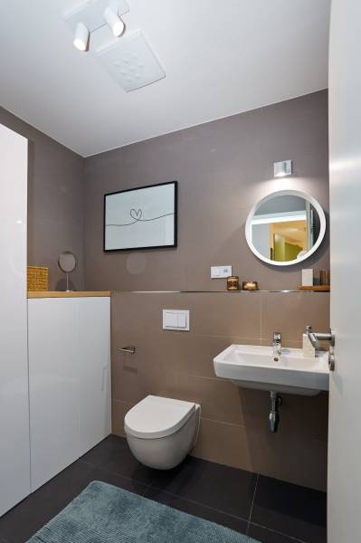 Bathroom with a sink, toilet, round mirror, and decorative painting in a 2-room apartment.