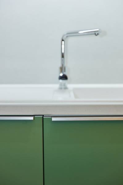 A kitchen cabinet with green doors and a chrome faucet in a 2-room apartment.