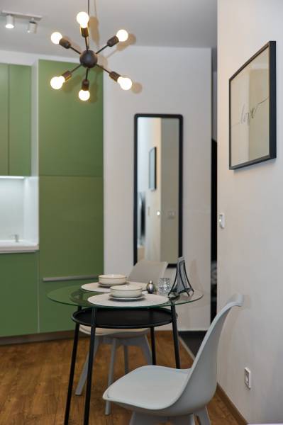 Dining area in a 2-room apartment, green cabinets, modern lighting, glass table, wooden decor flooring.
