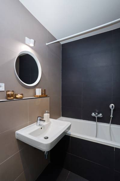 A bathroom in a 2-room apartment with a bathtub, a sink, and a round mirror above the sink.