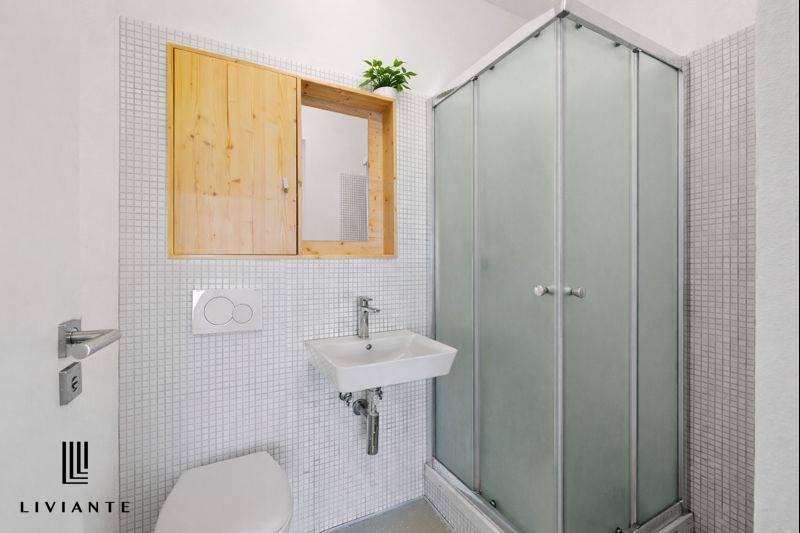 Bathroom in a building with white tiles, a shower stall, and a simple sink.