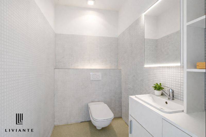 A bathroom with a sink, mirror, and toilet in a building. Minimalist design with muted colors.