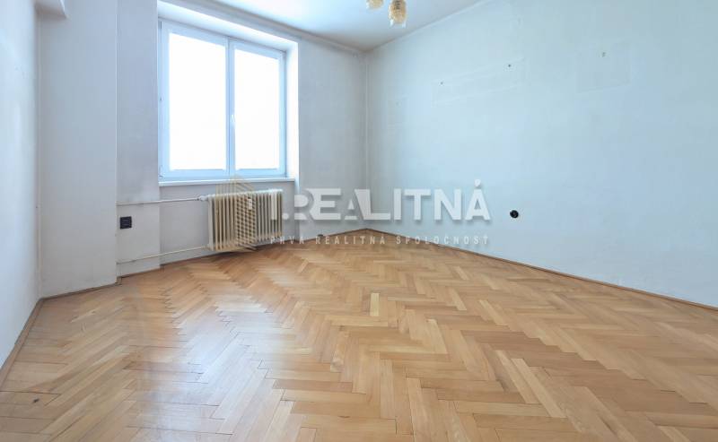 An empty room with a wood-patterned floor in a two-room apartment.