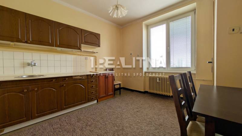 A kitchen with a brown cabinet and a table in a two-room apartment, colorful carpet.