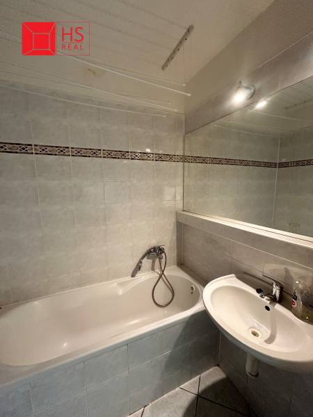 A bathroom with a bathtub and a sink in a 3-room apartment with tiled flooring.