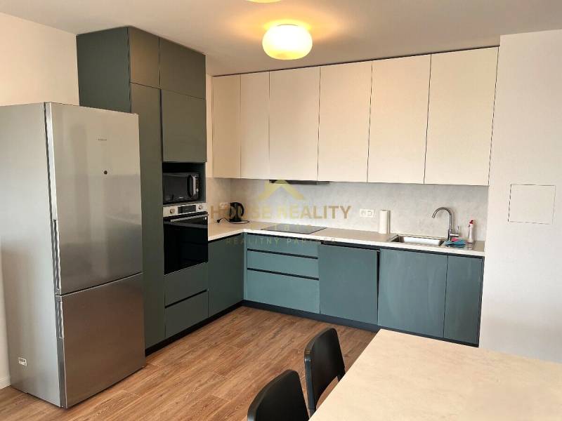 Straight kitchen unit with a refrigerator and appliances in a 2-room apartment with a wooden decor floor.