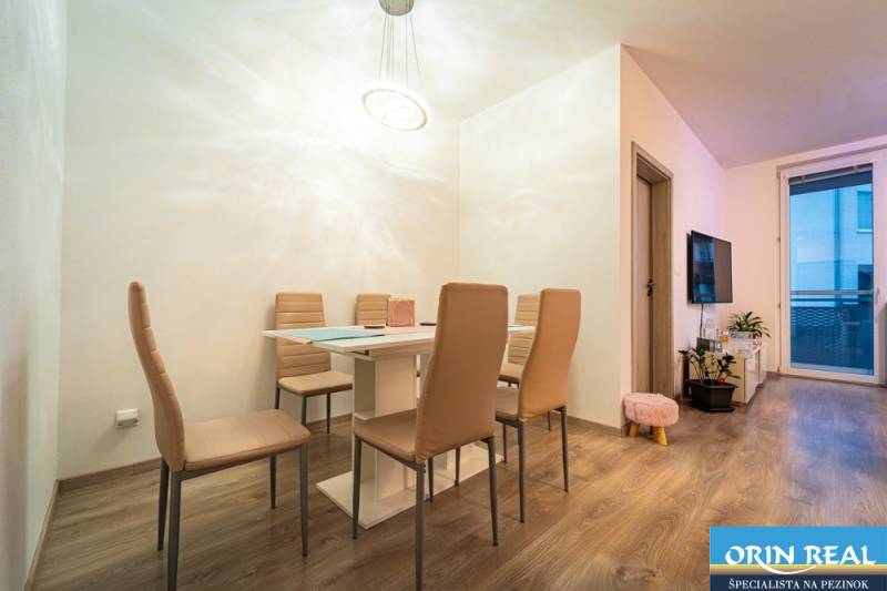 Dining area with a table and six chairs, wooden decor flooring in a 2-room apartment.