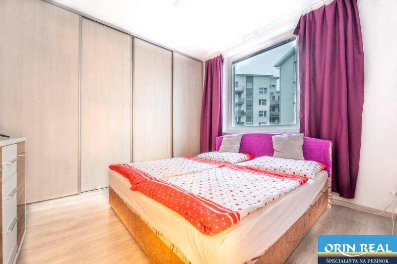 Bedroom in a 2-room apartment with wood-patterned flooring, a bed, and wardrobes.