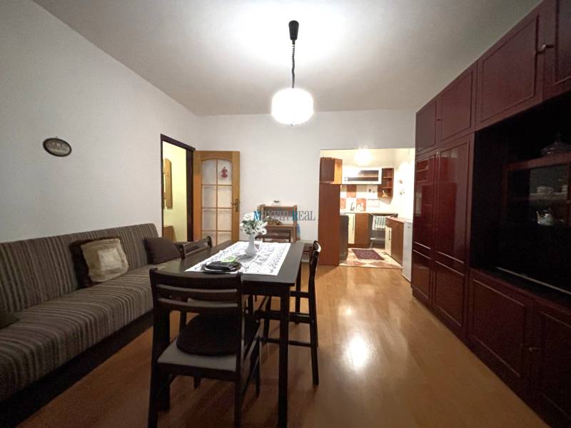 A two-room apartment with a wooden floor, a dining table, and a kitchen in the background.