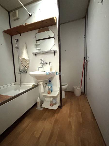Bathroom in a studio apartment with a bathtub, sink, and floor with wooden decor.