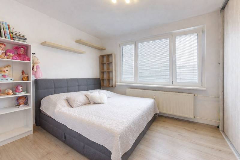 Bedroom with a bed, toys, and shelves in a 3-room apartment, floor with wood decor.