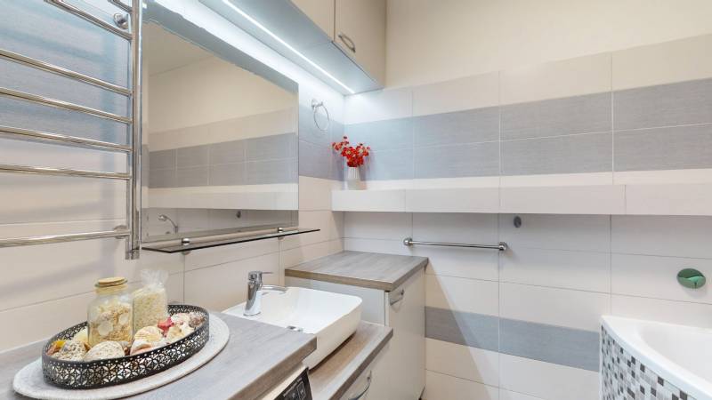 Bathroom in a 3-room apartment with white tiles and elegant decoration on the shelf.