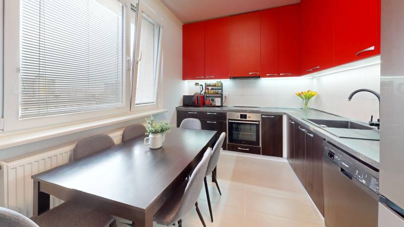 A kitchen in a 3-room apartment with red cabinets and a dining table.