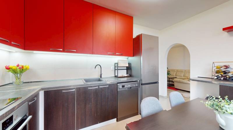 A kitchen unit with red cabinets, a dining table, and a view into the living room in a 3-room apartment.