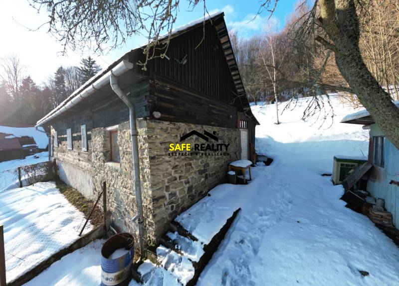 A cottage in Veľké Rovné in a snowy setting with stone walls and a wooden roof.
