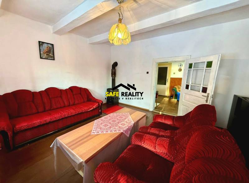 Living room in a cottage with a red sofa, chandelier, and wooden decor flooring.