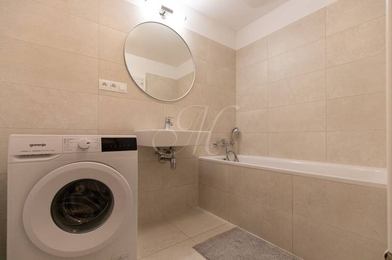 Bathroom in a 2-room apartment with a washing machine, bathtub, and beige tiles.