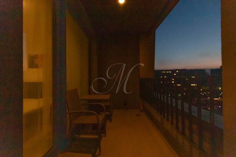 A night balcony with a view of the glowing city, chairs and a table for relaxation.